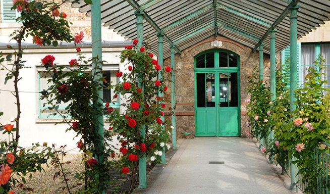 porte verte au fond d'une allée couverte avec haies de rosiers