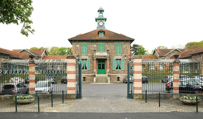 un portail d'entrée qui donne sur une maison en pierre avec des volets verts